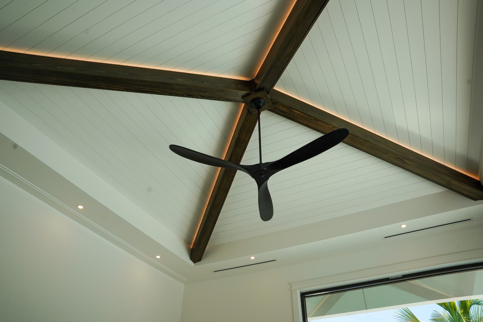 Vaulted ceiling with cove lighting along wood beams and a black three-blade ceiling fan