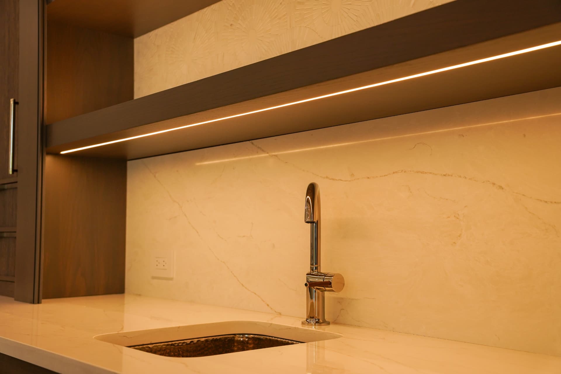 Linear LED under-cabinet lighting above a wet bar with stone backsplash