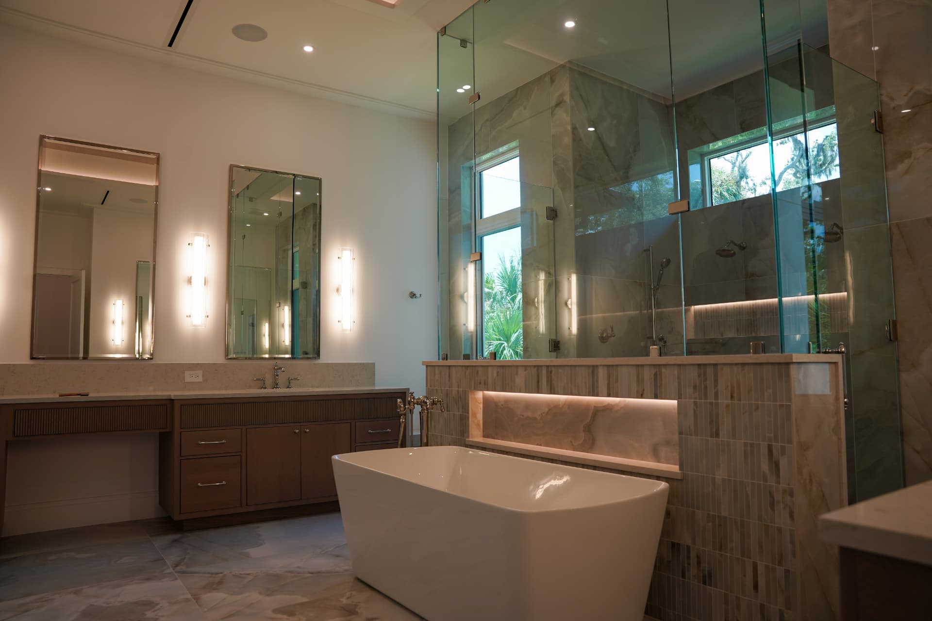 Primary bathroom with vanity sconces, recessed shower lighting, and a backlit stone niche